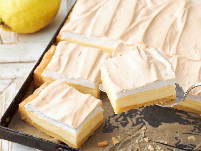 Zitronen-Schmand-Kuchen mit Baiser in einem dunklen Blech auf einem hellen Tisch mit frischen Zitronen.  | © StockFood / StockFood Studios / Brachat, Oliver