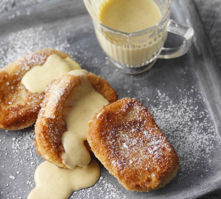 Auf einem Teller liegt eine Portion betrunkener Mönch mit Vanillesauce. Sie sind mit Puderzucker bestreut. | © StockFood / für ZS Verlag / Kramp + Gölling