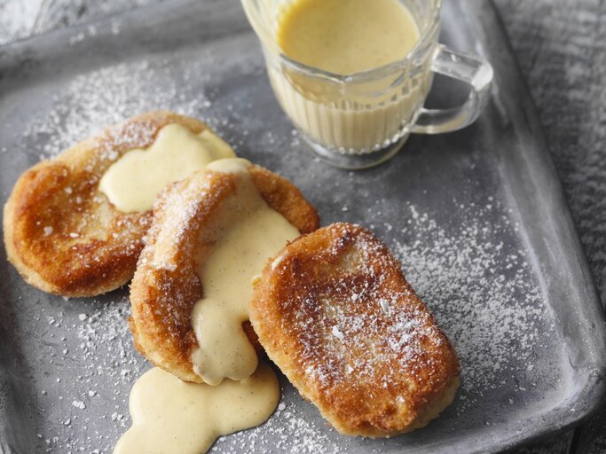 Auf einem Teller liegt eine Portion betrunkener Mönch mit Vanillesauce. Sie sind mit Puderzucker bestreut. | © StockFood / für ZS Verlag / Kramp + Gölling