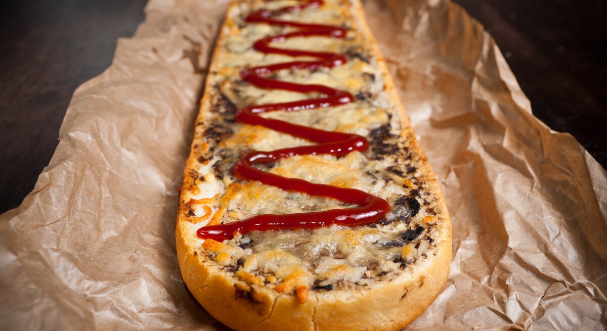 Polnisches Baguette überbacken mit Pilzen, Zwiebeln und Käse, garniert mit Ketchup.