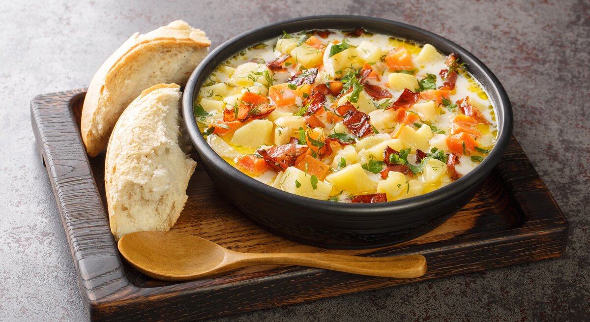 Polnische Kartoffelsuppe Kartoflanka mit Brot und Holzlöffel auf Holzbrett auf grauem Untergrund. Draufsicht.