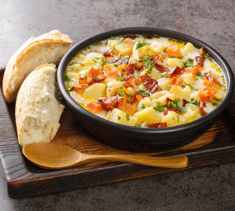 Polnische Kartoffelsuppe Kartoflanka mit Brot und Holzlöffel auf Holzbrett auf grauem Untergrund. Draufsicht. | © Getty Images / ALLEKO