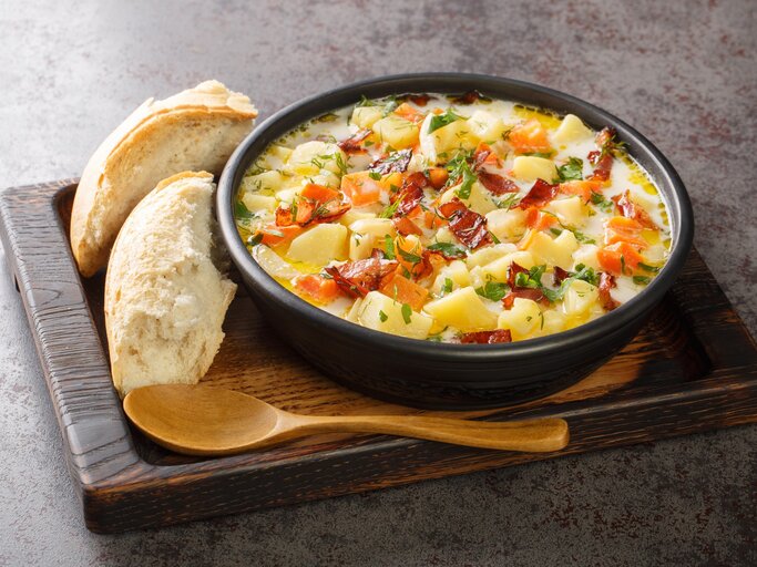 Polnische Kartoffelsuppe Kartoflanka mit Brot und Holzlöffel auf Holzbrett auf grauem Untergrund. Draufsicht. | © Getty Images / ALLEKO