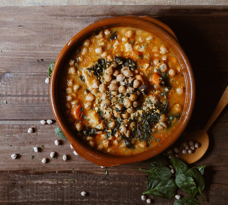 Eine Schale Mangold-Curry mit Kichererbsen in der Draufsicht, daneben ein Holzlöffel und ein paar Kichererbsen und Mangoldblätter. | © Shutterstock/ EGHStock