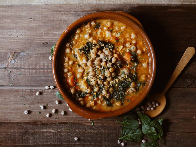 Eine Schale Mangold-Curry mit Kichererbsen in der Draufsicht, daneben ein Holzlöffel und ein paar Kichererbsen und Mangoldblätter. | © Shutterstock/ EGHStock