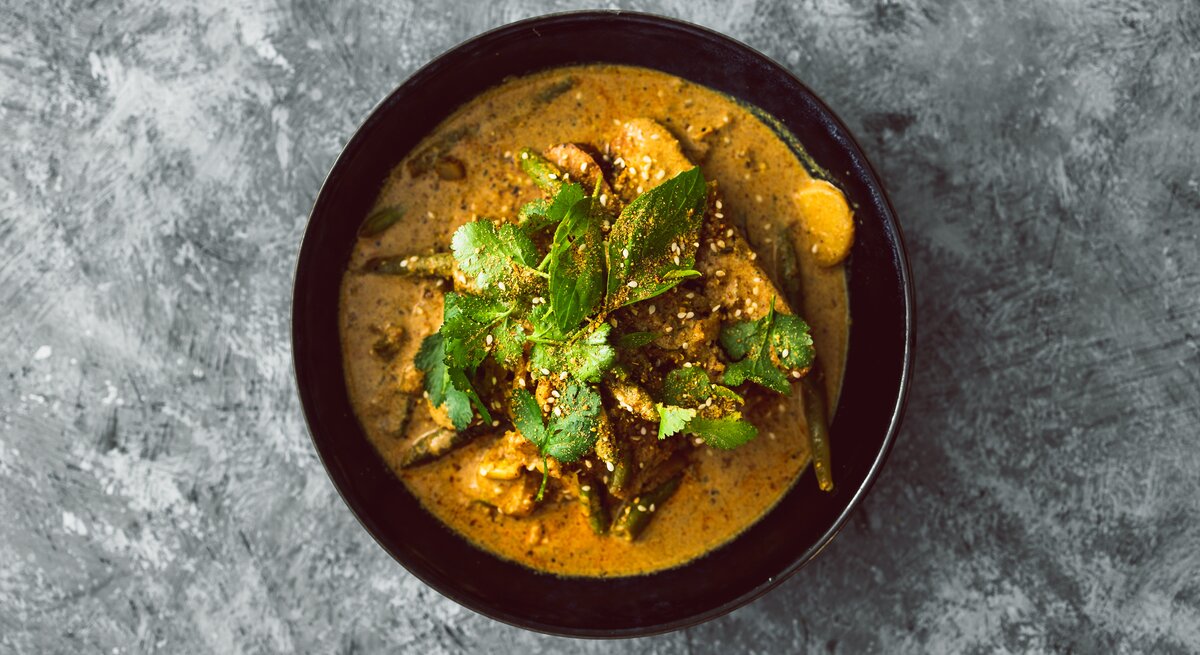 Draufsicht: eine schwarze Schüssel Koriander-Curry mit Tofu steht auf einem grau-weißem Untergrund.