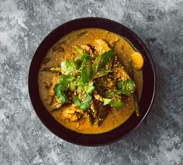 Draufsicht: eine schwarze Schüssel Koriander-Curry mit Tofu steht auf einem grau-weißem Untergrund. | © Shutterstock / faithie