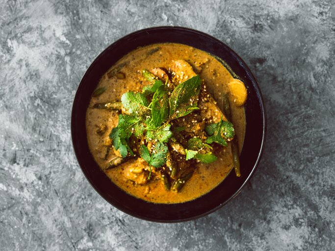 Draufsicht: eine schwarze Schüssel Koriander-Curry mit Tofu steht auf einem grau-weißem Untergrund. | © Shutterstock / faithie