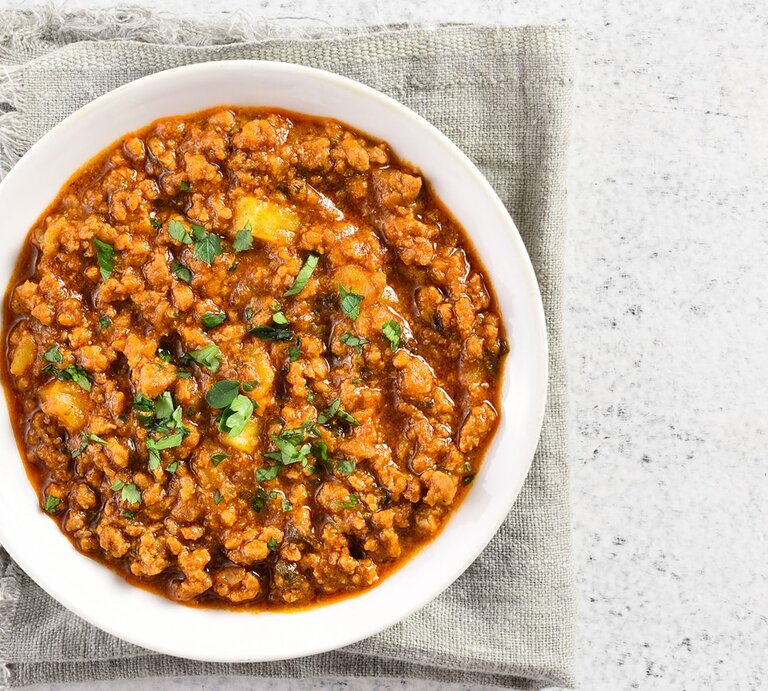 Eine weiße Schale mit dem rötlichen Curry auf einem hell-beigenen Leinentuch und einem weißen Tisch. | © Shutterstock/ Tatiana Volgutova