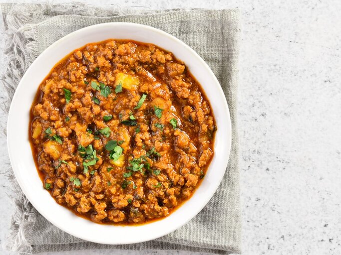 Eine weiße Schale mit dem rötlichen Curry auf einem hell-beigenen Leinentuch und einem weißen Tisch. | © Shutterstock/ Tatiana Volgutova
