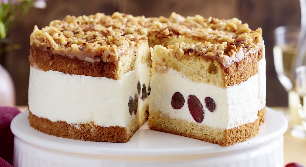 Angeschnittene Weißwein-Trauben-Torte auf weißem Tortenteller, verschwommener Hintergrund. 