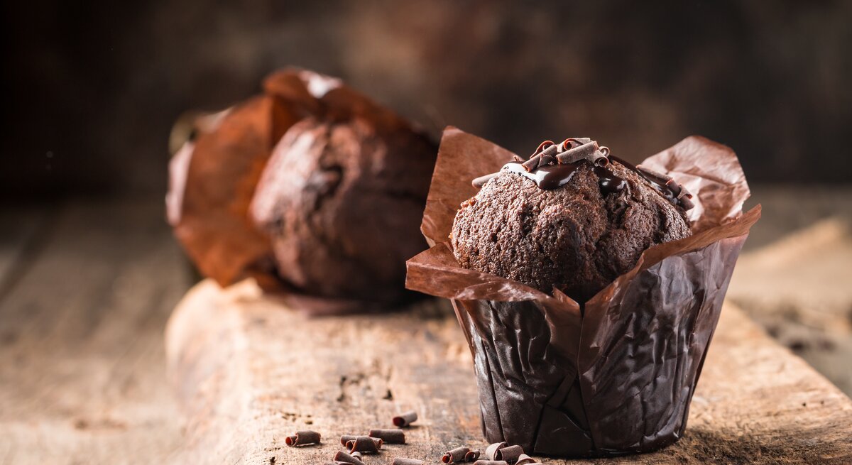 Auf einem Brett stehen zwei Schoko-Rotwein-Muffins, daneben liegen ein paar Schokosplitter.