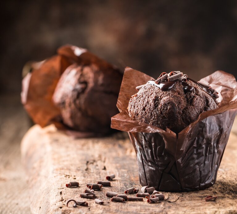 Auf einem Brett stehen zwei Schoko-Rotwein-Muffins, daneben liegen ein paar Schokosplitter. | © Shutterstock/ Goskova Tatiana