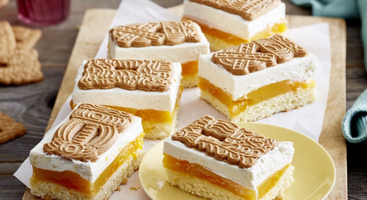 Auf einem Brett liegen mehrere Mandarinen-Spekulatius-Schnitten. Sie sind cremig und haben mehrere Schichten.