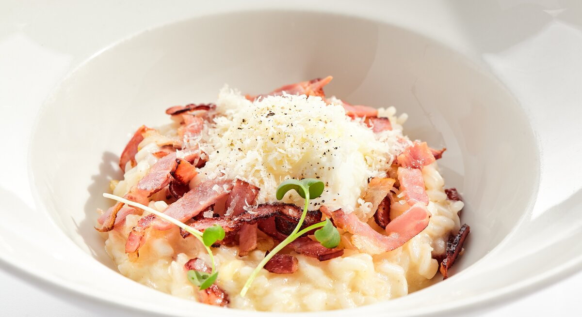 Risotto mit Speck und geriebenem Käse auf weißem Teller. 