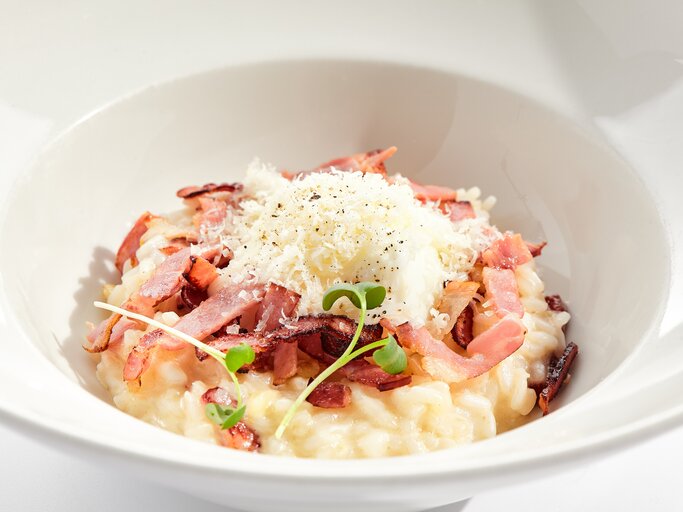 Risotto mit Speck und geriebenem Käse auf weißem Teller.  | © Getty Images/Ryzhkov