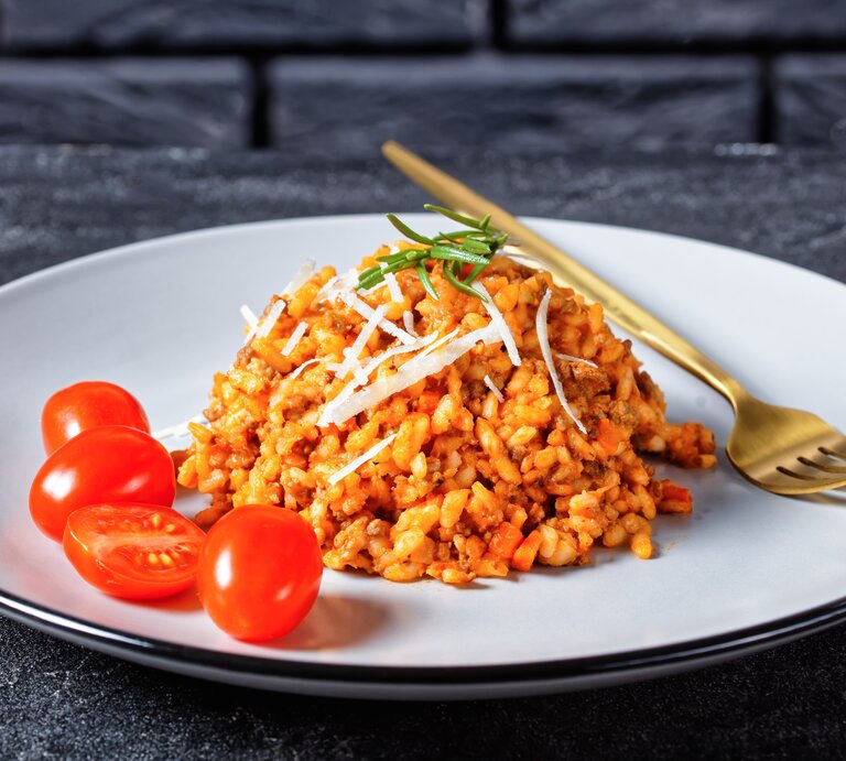 Hackfleisch-Risotto mit Cocktailtomaten auf weißem Teller mit Kupfergabel auf dunklem Untergrund. Draufsicht. | © shutterstock / from my point of view