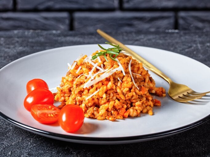 Hackfleisch-Risotto mit Cocktailtomaten auf weißem Teller mit Kupfergabel auf dunklem Untergrund. Draufsicht. | © shutterstock / from my point of view