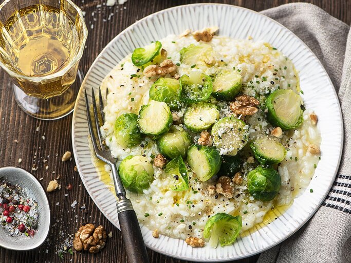 Ein Teller Rosenkohl-Risotto mit Walnüssen, daneben eine Gabel und ein Glas Wein. | © StockFood / Schall, Ewgenija