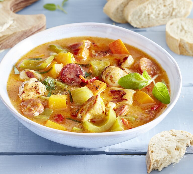 Hähnchen-Kürbis-Gulasch in einem weißten tiefen Teller. Daneben liegt Brot und ein Holzbrett.  | © EAT CLUB / Isabell Triemer