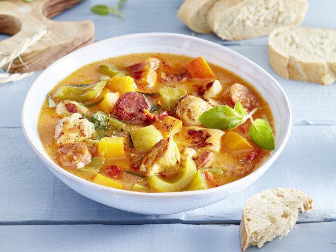 Hähnchen-Kürbis-Gulasch in einem weißten tiefen Teller. Daneben liegt Brot und ein Holzbrett.  | © EAT CLUB / Isabell Triemer