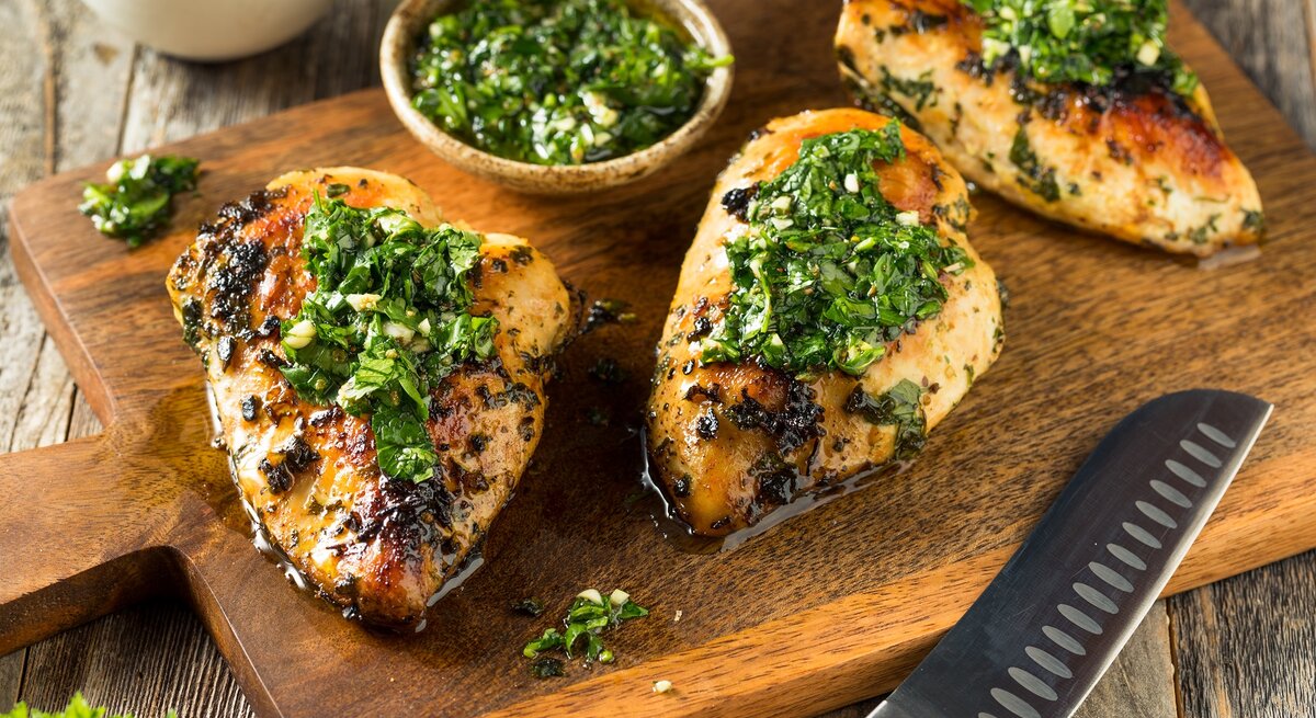 Ein Holzbrett mit Chimichurri-Hähnchen neben einem Messer.
