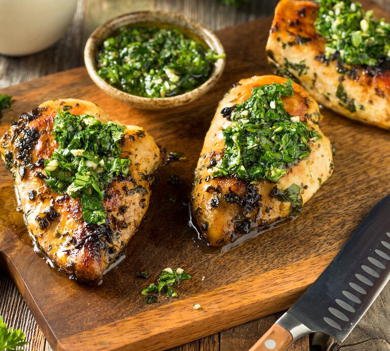 Ein Holzbrett mit Chimichurri-Hähnchen neben einem Messer. | © AdobeStock/Brent Hofacker