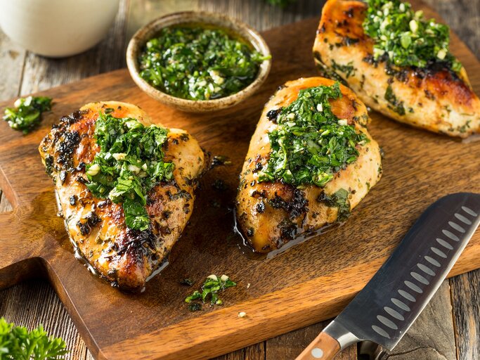 Ein Holzbrett mit Chimichurri-Hähnchen neben einem Messer. | © AdobeStock/Brent Hofacker