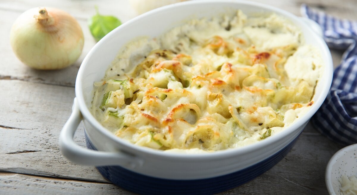 Blumenkohl-Zwiebel-Gratin in weißer Auflaufform auf hölzernem Untergrund. 