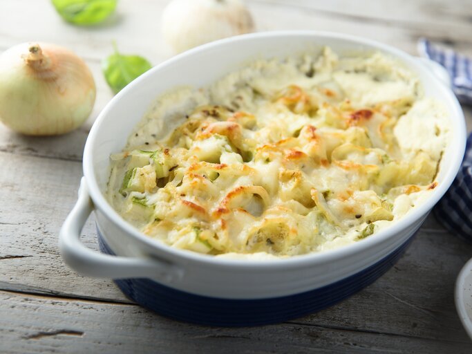 Blumenkohl-Zwiebel-Gratin in weißer Auflaufform auf hölzernem Untergrund.  | © Getty Images/Mariha-kitchen