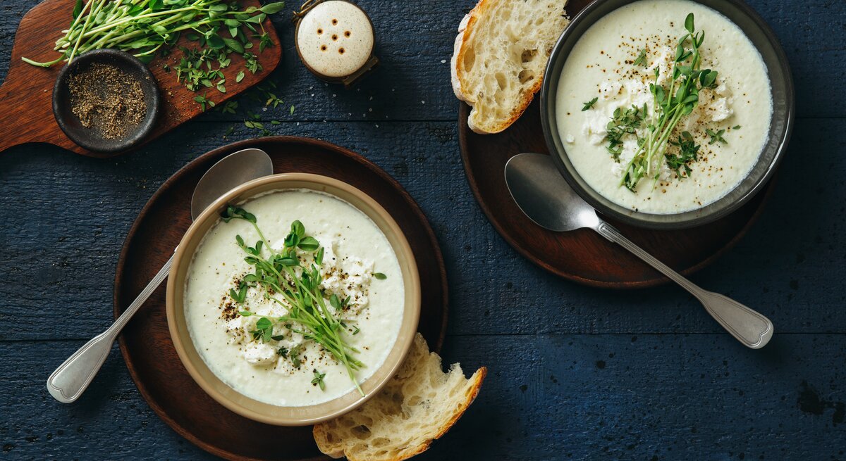 Blumenkohl-Feta-Suppe mit frischem Majoran belegt auf blauem Untergrund. 