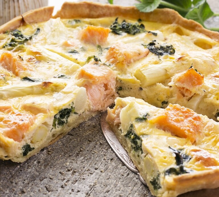 Die portionierte Quiche auf einem Steintisch mit einem Tortenheber, der ein Stück etwas anhebt. Im Hintergrund Vasen und Pflanzen. | © Shutterstock/ hlphoto