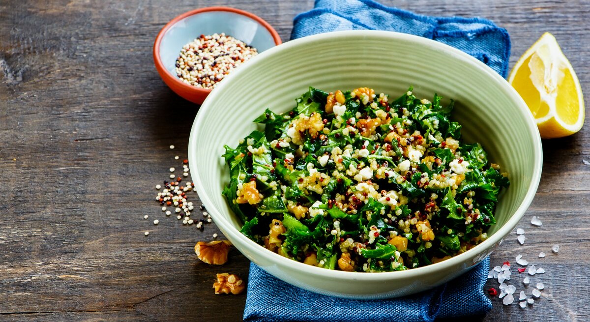 Eine Schüssel Grünkohlsalat mit Walnüssen, daneben eine Zitronenspalte und eine Schale mit Kernen.