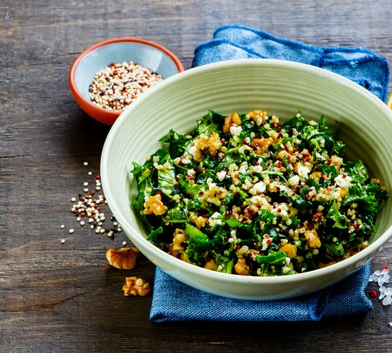 Eine Schüssel Grünkohlsalat mit Walnüssen, daneben eine Zitronenspalte und eine Schale mit Kernen. | © Shutterstock/ Yuliya Gontar