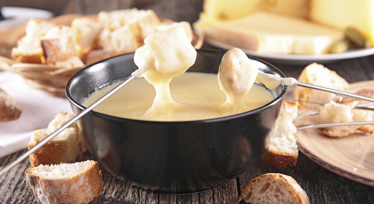 Mehrere Brotstücke die in eine Schale voll Käsefondue getunkt werden.