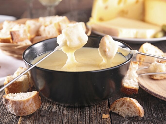 Mehrere Brotstücke die in eine Schale voll Käsefondue getunkt werden. | © iStock/ margouillatphotos