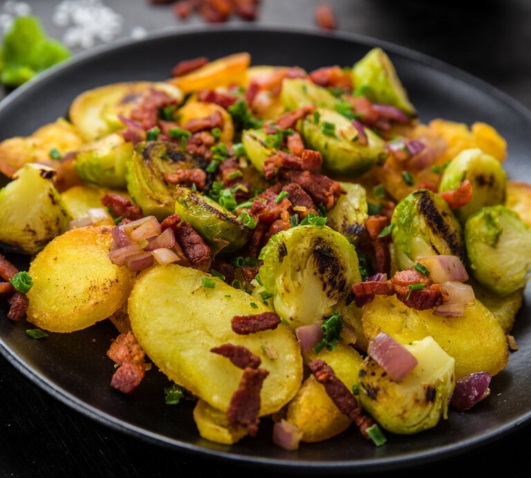 Ein schwarzer Teller mit Gröstl mit Rosenkohl auf einem schwarzen Tisch. | © AdobeStock/Fischer Food Design