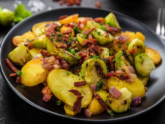 Ein schwarzer Teller mit Gröstl mit Rosenkohl auf einem schwarzen Tisch. | © AdobeStock/Fischer Food Design