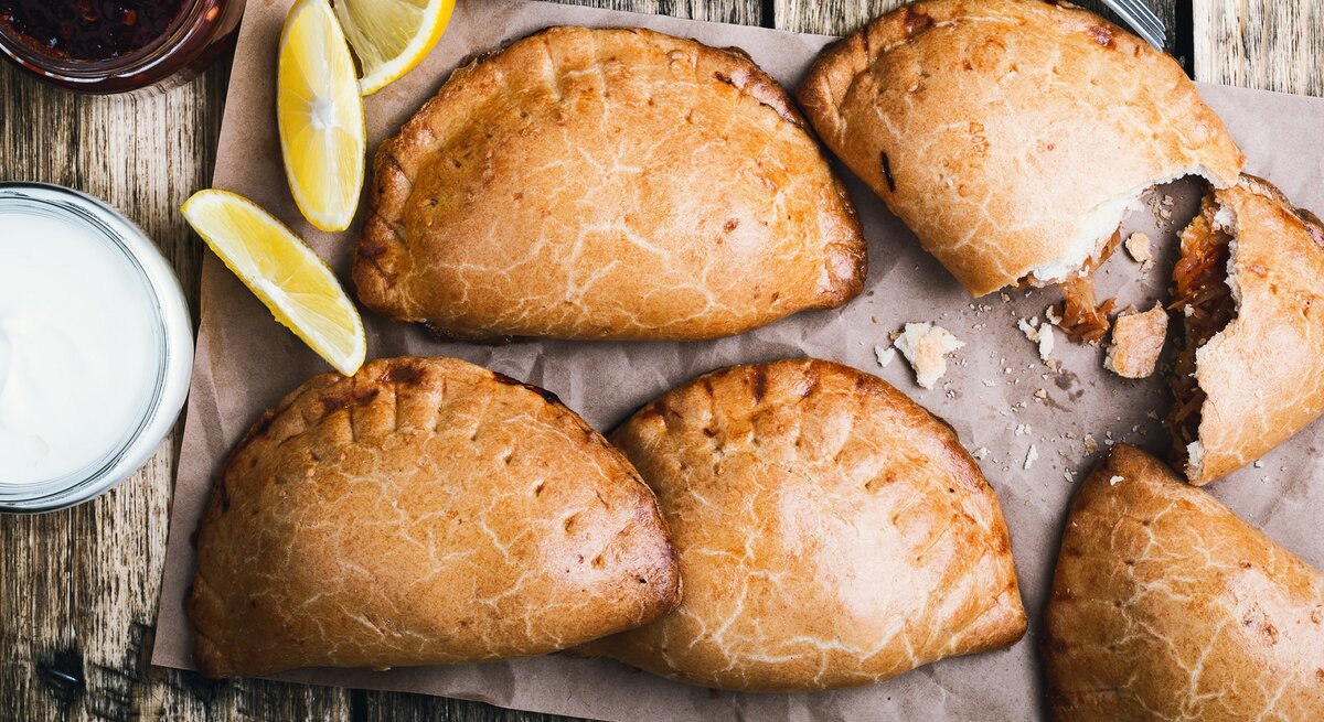 Empanadas nach mexikanischer Art auf einem Backpapier. Daneben Zitronen. 