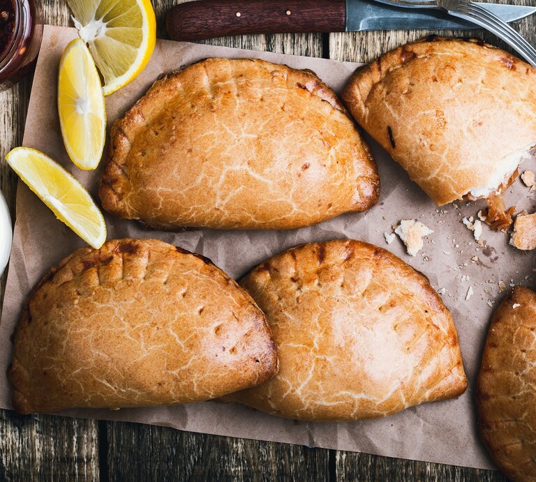 Empanadas nach mexikanischer Art auf einem Backpapier. Daneben Zitronen.  | © Getty Images /istetiana
