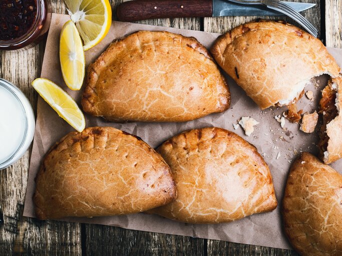 Empanadas nach mexikanischer Art auf einem Backpapier. Daneben Zitronen.  | © Getty Images /istetiana