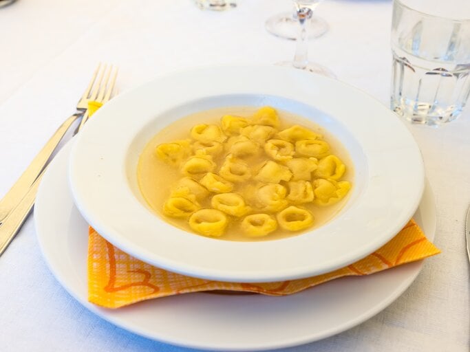 Teller mit klarer Brühe und Tortellini auf weißem Tischtuch.  | © Shutterstock/FPWing