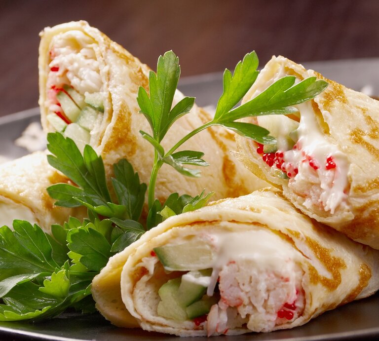 Vier angeschnittene Wraps mit Flusskrebs, Mayonnaise und Gurke auf einem grauen Teller und einem dunklen Holzuntergrund. | © Shutterstock/ Fanfo