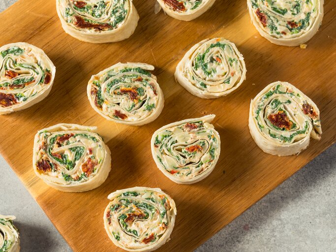 Wrap-Röllchen mit Feta, Spinat & getrockneten Tomaten auf Holzbrett.  | © Getty Images/bhofack2