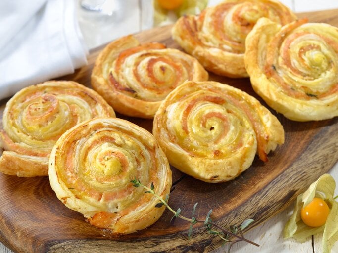 Sechs Blätterteigschnecken mit Lachs angerichtet auf einem Holzbrett.  | © Getty Images/kabVisio