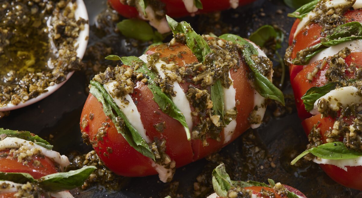 Fächer-Tomaten a la Caprese mit Knoblauch-Pesto serviert.