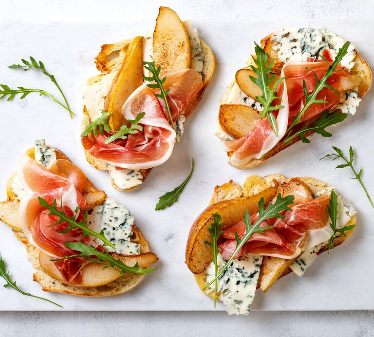 Crostini mit Birne, Schinken und Gorgonzola auf einer grauen Keramik-Platte.  | © Getty Images/ sveta_zarzamora