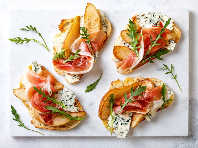 Crostini mit Birne, Schinken und Gorgonzola auf einer grauen Keramik-Platte.  | © Getty Images/ sveta_zarzamora