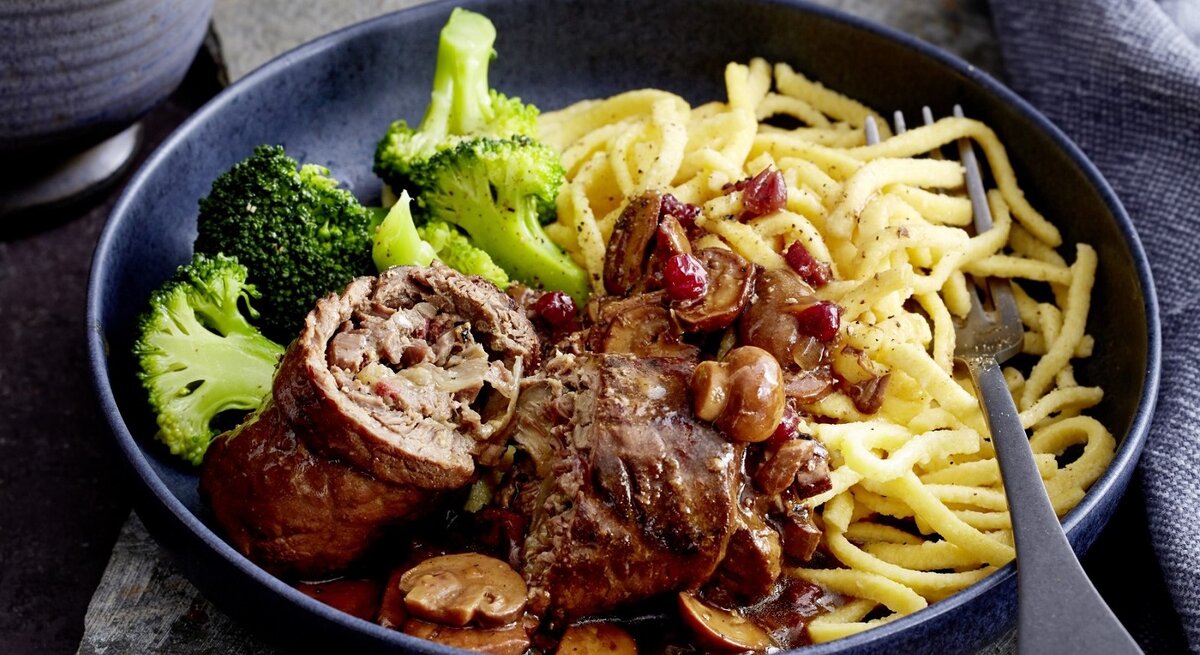Auf einem tiefen Teller liegt eine Portion Rinderrouladen mit Pilzen und Spätzle. Sie wird mit Brokkoli serviert.