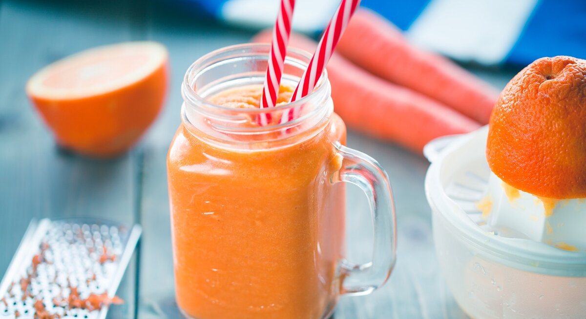 Ein Glas mit dem Karotten-Orangen-Smoothie auf einem dunkelblauen Tisch.
